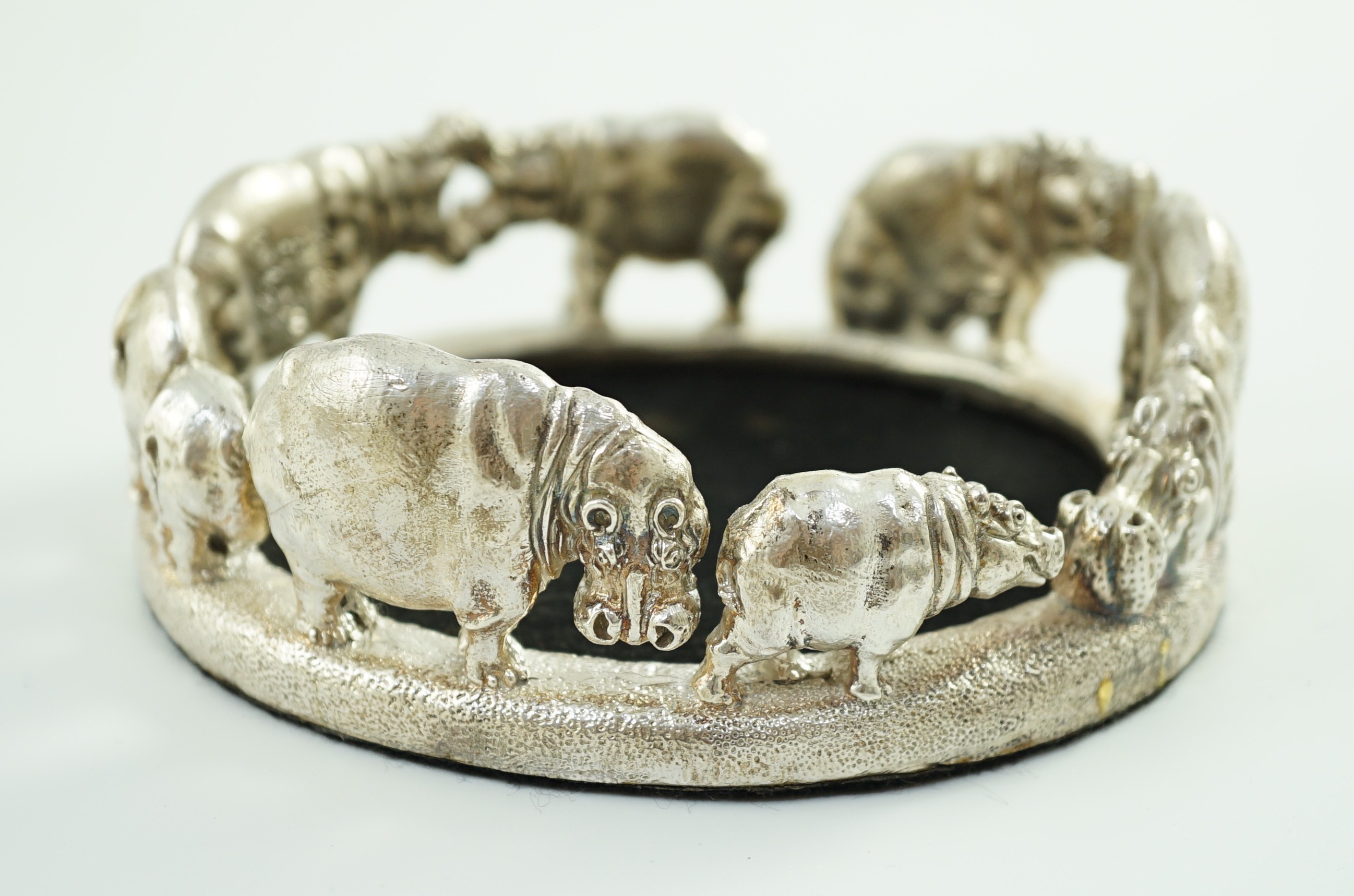 Patrick Mavros - A modern novelty silver bottle coaster, modelled as a continuous bloat of hippopotami, in various positions